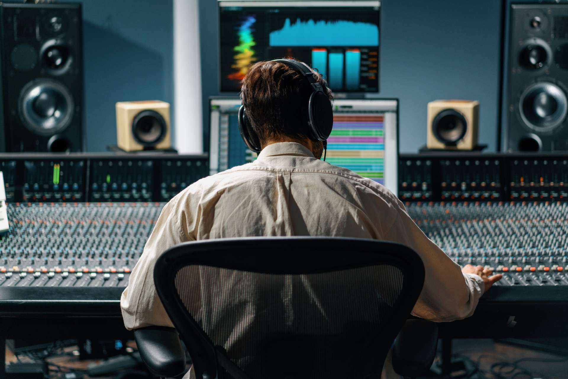 Un ingeniero de sonido con audífonos frente a una consola de mezcla grande, trabajando una sesión de postproducción en un estudio con monitores y bocinas.
